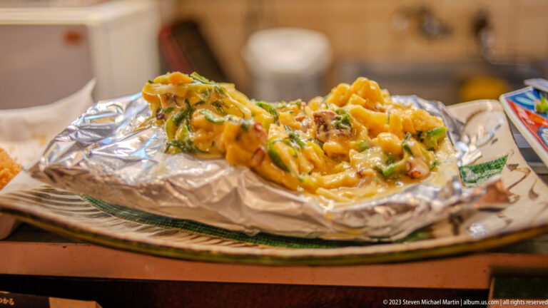 Cheese-topped hot dish with chopped greens served on foil in an Osaka restaurant.