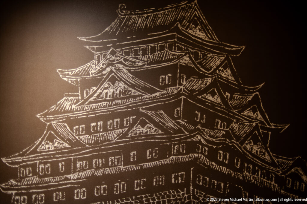 White line drawing of Osaka Castle’s multi-tiered keep on a dark background.