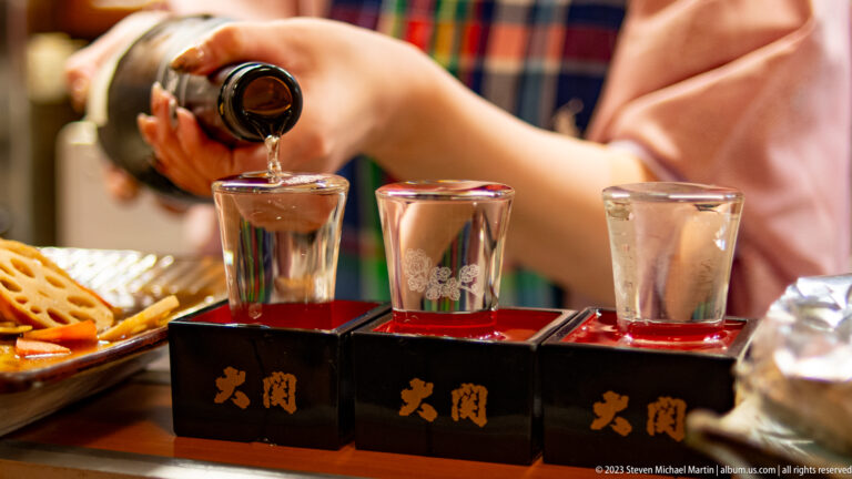 Sake being poured into a small glass set inside a square masu box.