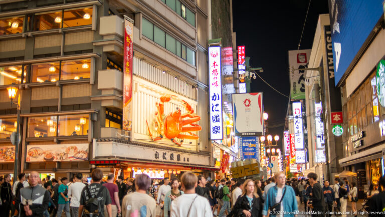 Crowded Dotonbori street beneath the giant Kani Doraku crab sign.