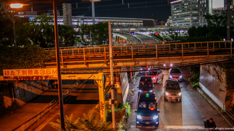 Cars pass beneath an orange-lit Osaka overpass marked with a 3.6-metre clearance sign.