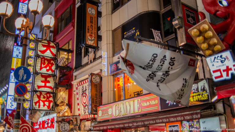 Upward view of giant restaurant signs, including a pufferfish, in Dotonbori.