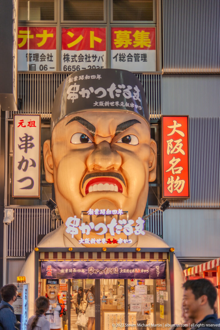 Giant Kushikatsu Daruma mascot head above an Osaka restaurant entrance.