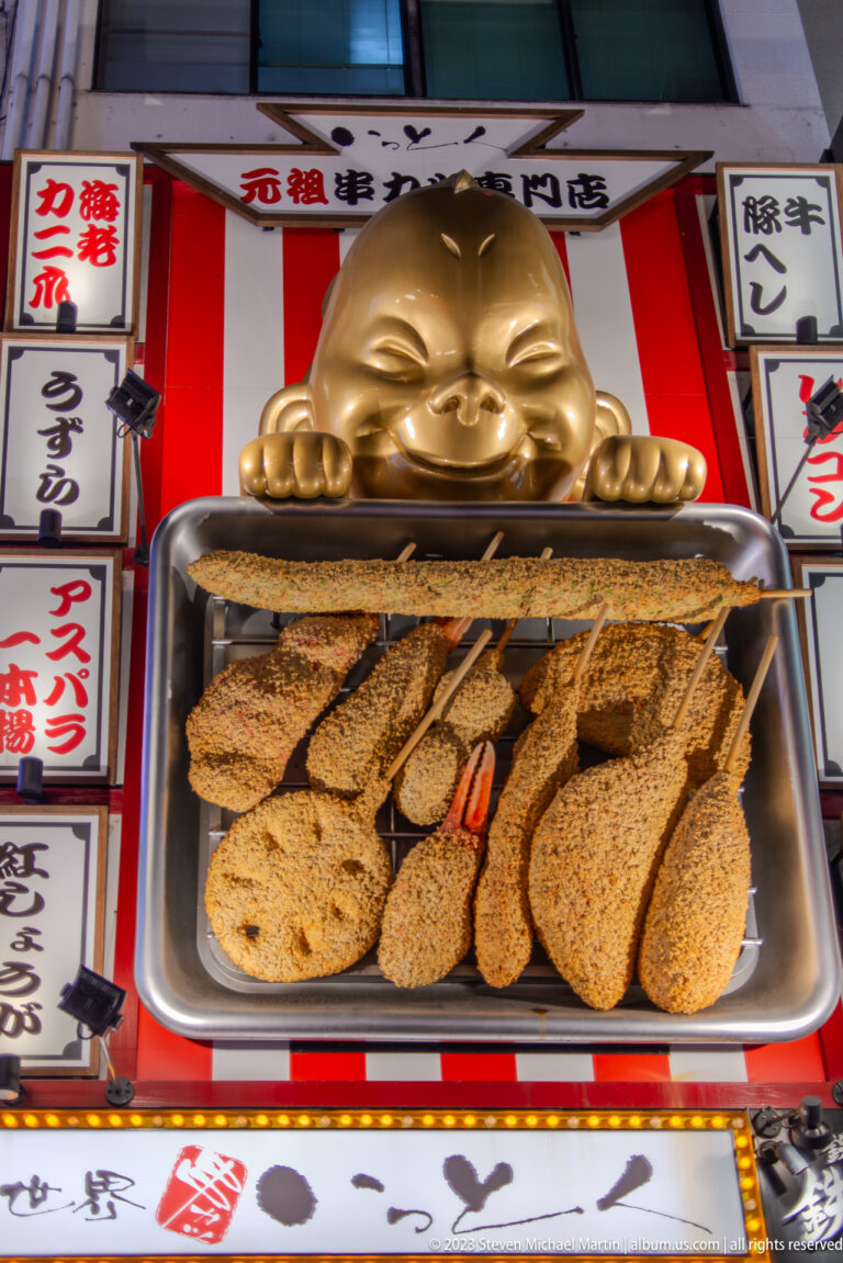 Oversized breaded kushikatsu skewers displayed beneath a gold restaurant mascot.