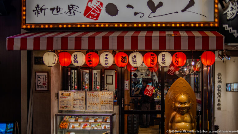 Osaka kushikatsu restaurant entrance with lanterns, striped awning, and gold mascot.
