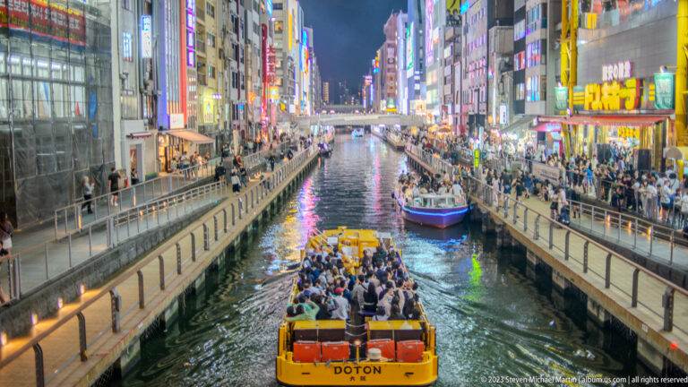 Passenger sightseeing boats traveling through the illuminated Dotonbori Canal.