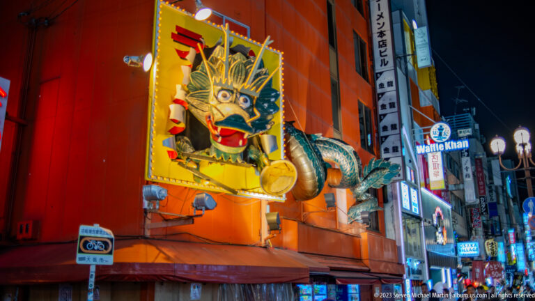 Large three-dimensional dragon projecting from a red Dotonbori restaurant façade.