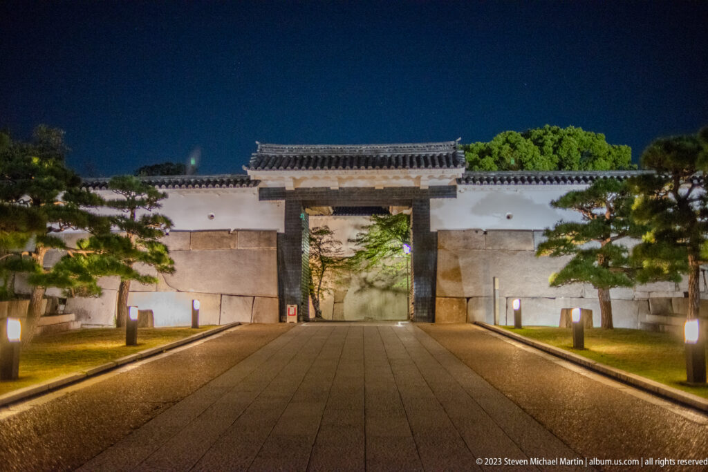 Illuminated gate in white plaster walls along a stone path at Osaka Castle.