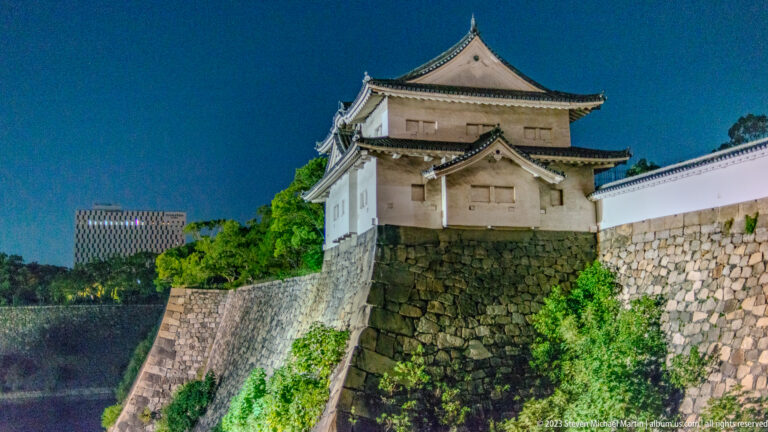 White Osaka Castle turret above massive stone foundations and plaster walls at night.