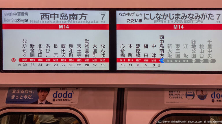 Bilingual Midosuji Line route map at Namba Station, marked M14, above train doors.