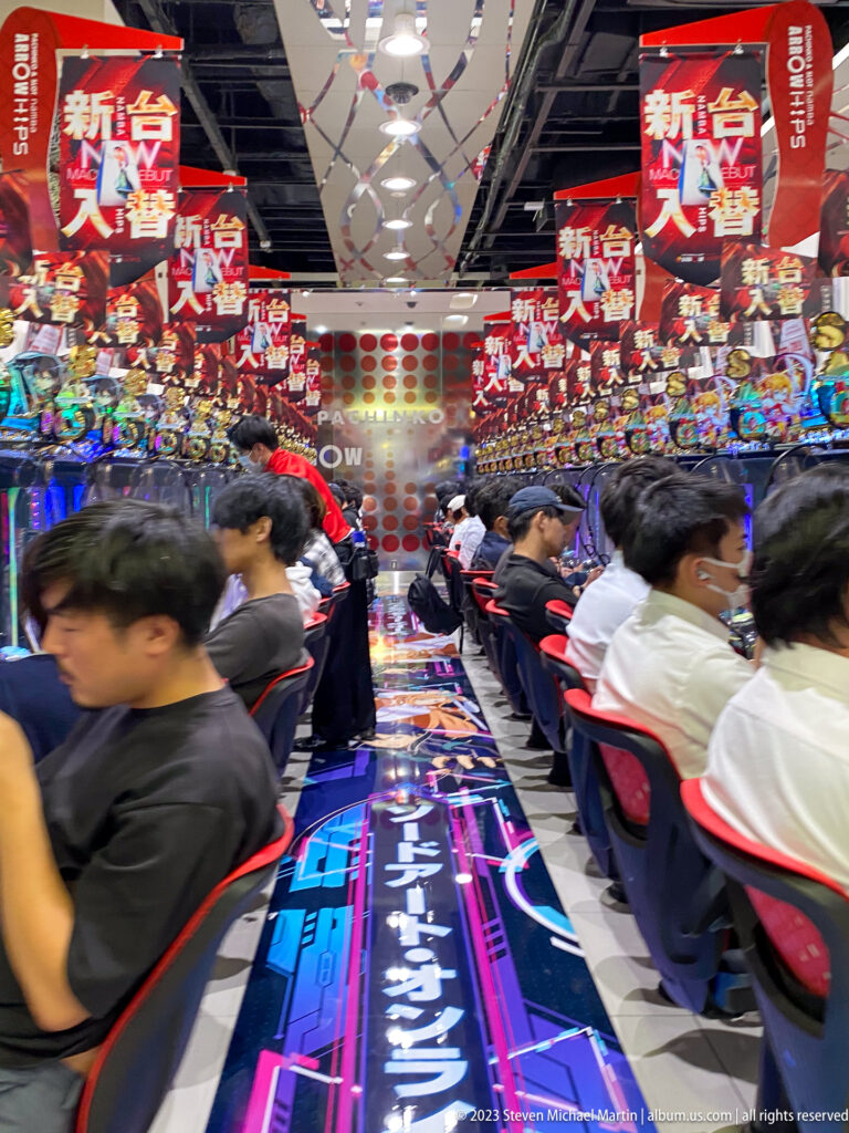 Players seated closely at brightly illuminated pachinko machines in Osaka.