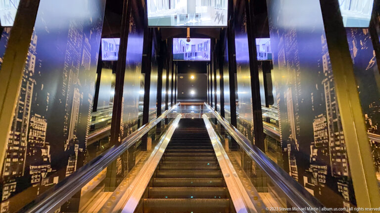 Escalator ascending between mirrored walls and black-and-white cityscape murals.