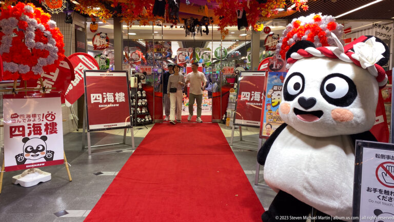 Large decorated panda mascot beside a red-carpeted Shinsaibashi commercial entrance.