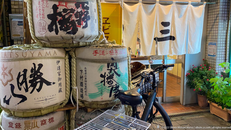 Stacked sake barrels, bicycle, and white noren curtains at an Osaka restaurant entrance.
