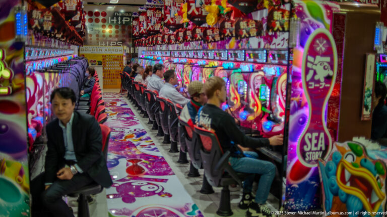 Rows of players seated at brightly illuminated pachinko machines in an Osaka parlor.