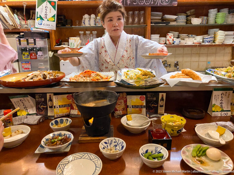 Restaurant server presenting two plates above a counter crowded with food.