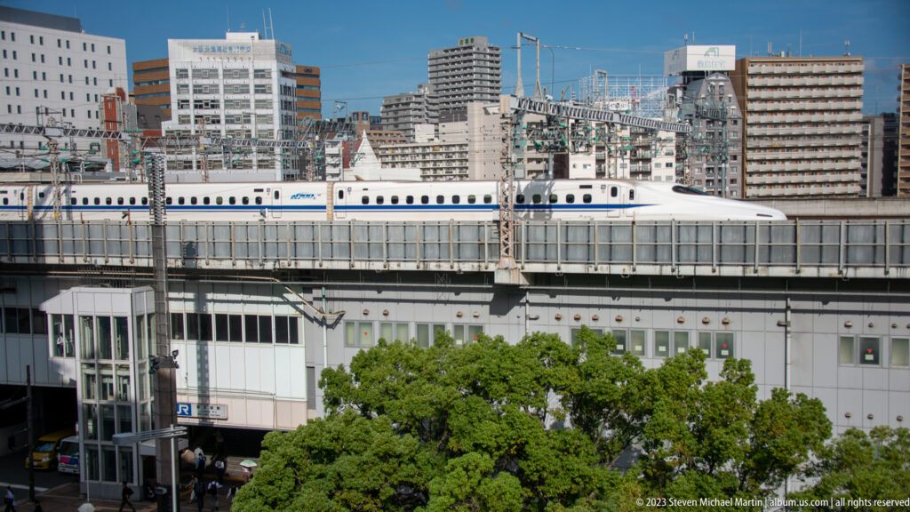 White Shinkansen traveling on elevated tracks through urban Osaka.