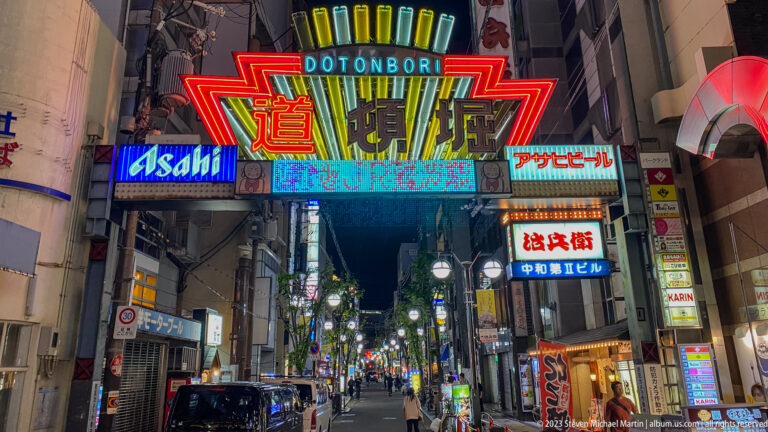 Bright Dotonbori gateway above a narrow neon-lit Osaka street.