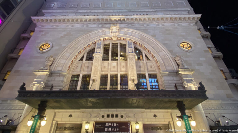 Illuminated historic stone façade with a large arched window and Japanese signs.