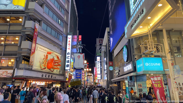 Pedestrians crowding Dotonbori beneath the Kani Doraku crab and bright signs.