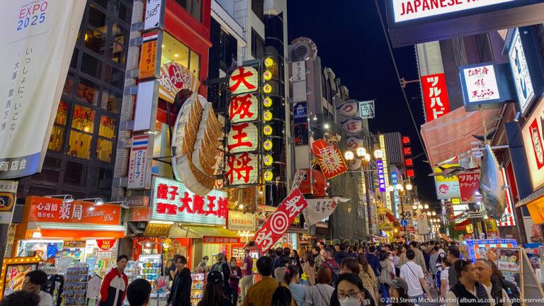 Crowded Dotonbori street beneath giant restaurant signs and illuminated vertical banners.