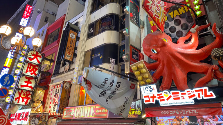 Large red octopus sign with curling tentacles above a Dotonbori street.