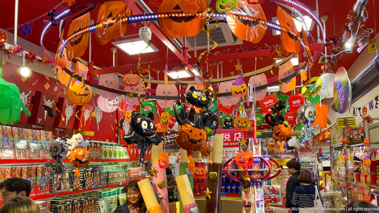 Shop interior crowded with hanging Halloween pumpkins, ghosts, and colorful decorations.