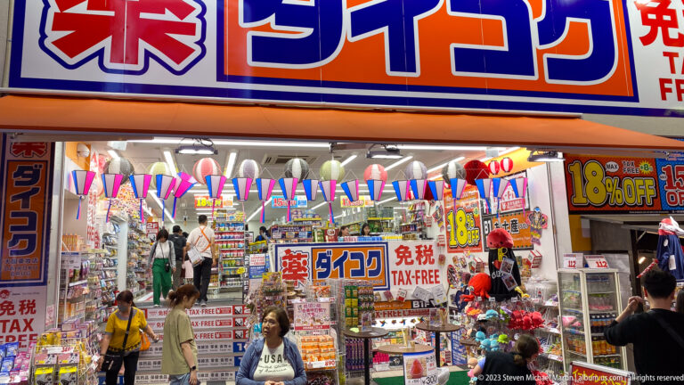 Daikoku Drug storefront with tax-free signs, discount posters, and crowded merchandise.