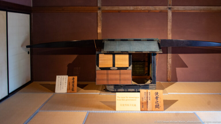 Historic Japanese palanquin with enclosed passenger box and long carrying poles displayed on tatami mats.