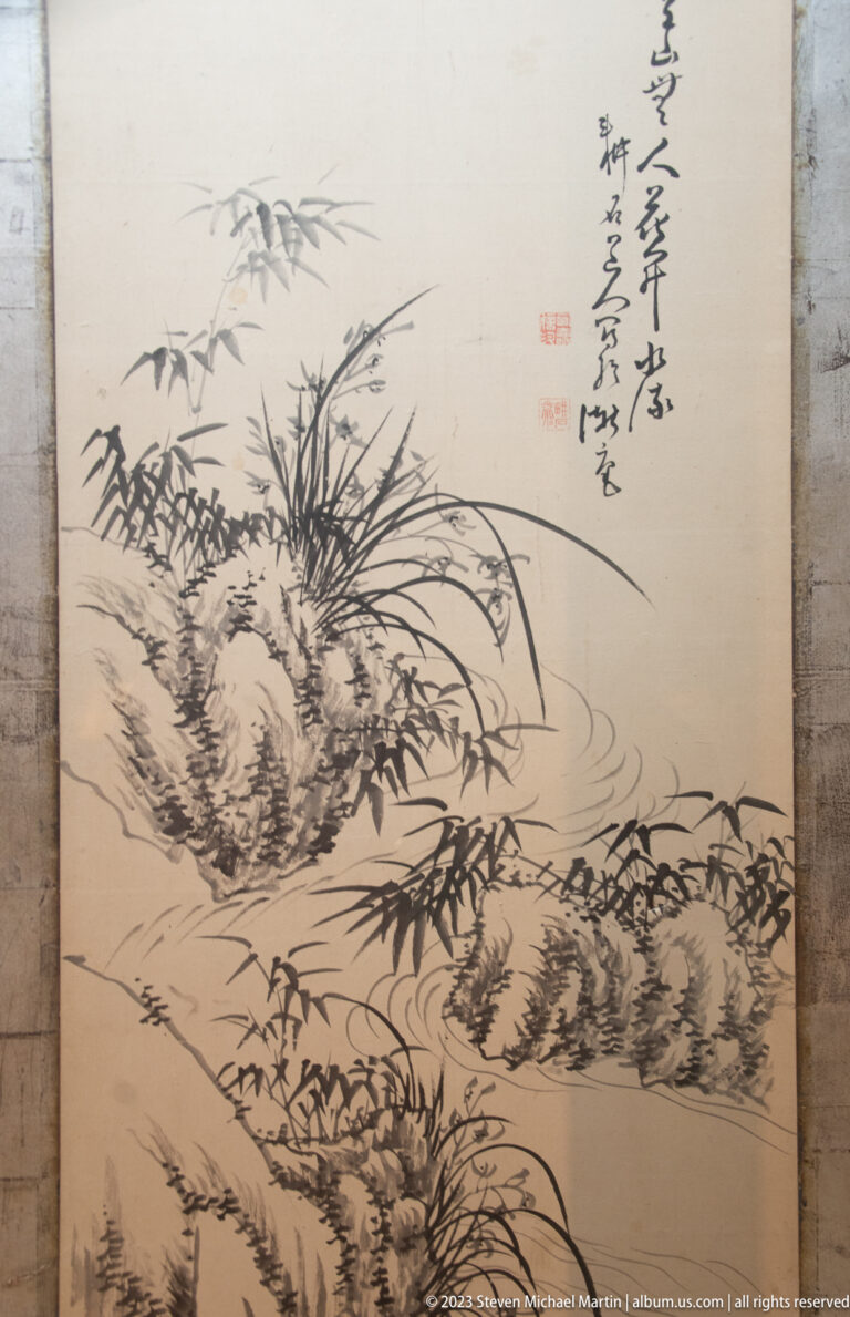 Monochrome Japanese ink painting of bamboo, grasses, rocks, and flowing water with calligraphy at upper right.