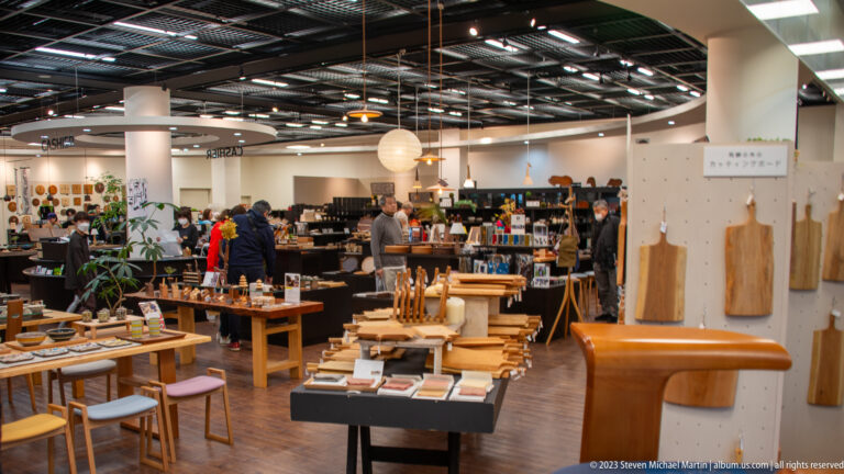 Bright modern shop interior with wooden cutting boards, utensils, baskets, furnishings, and design goods displayed on tables.