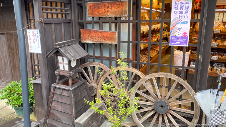 Weathered wooden cart with two large spoked wheels displayed beside a shop window and green plants.