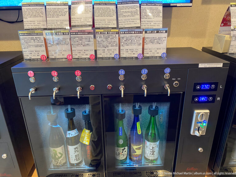 Black sake tasting machine with numbered taps, tasting cards, chilled bottles, and digital temperature displays.
