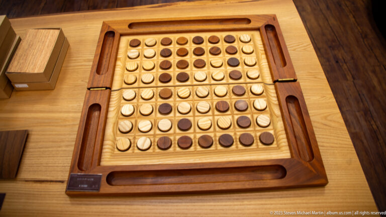 Wooden eight-by-eight Reversi board holds round light-and-dark discs, with storage channels built into the frame.