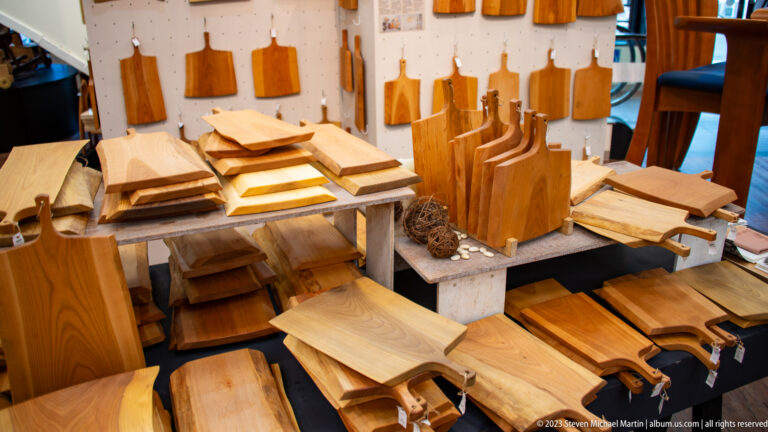 Wooden cutting boards, handled paddles, trays, and folded textiles crowd a low craft-store display.