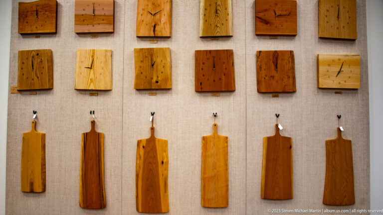 Wall display of rectangular wood samples above a row of narrow handcrafted wooden serving boards.