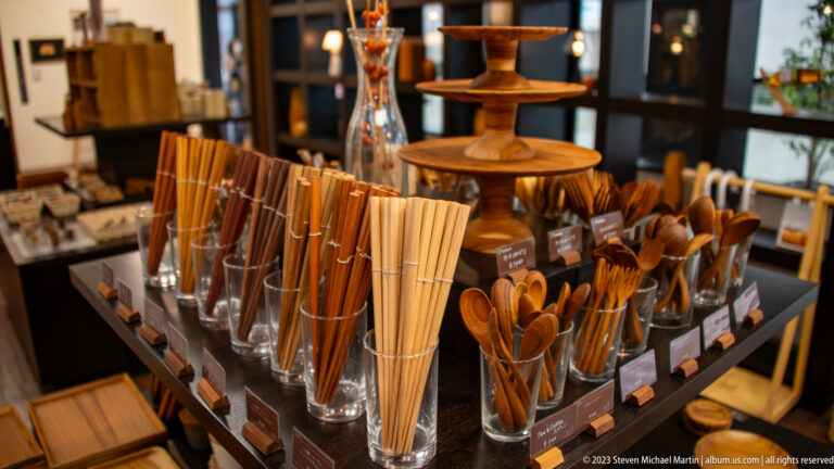 Bundles of chopsticks, wooden spoons, brushes, and small turned vessels fill glass containers around a tiered stand.
