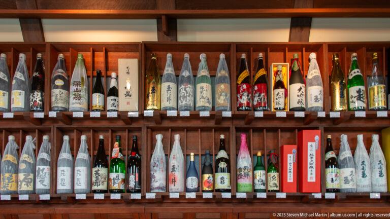 Japanese sake and other beverage bottles fill wooden shelves in varied shapes, labels, colors, and wrappings.