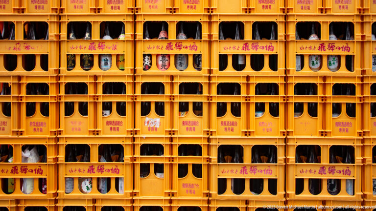 Wall of orange plastic beverage crates filled with dark returnable bottles and assorted Japanese labels.