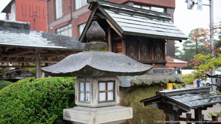 Close view of a weathered stone lantern with square chamber, broad cap, rounded finial, and mossy surfaces.