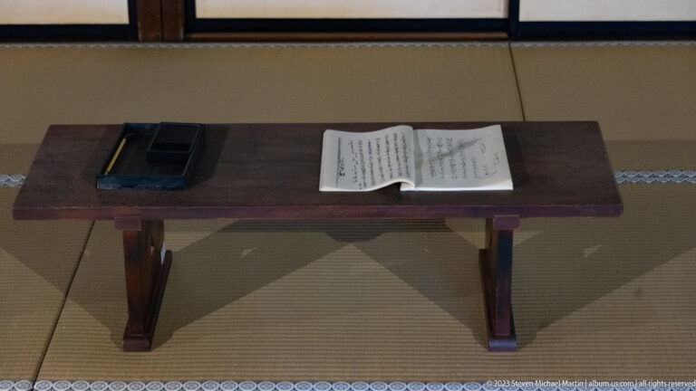 Low wooden desk on tatami with an inkstone box and open handwritten Japanese document.