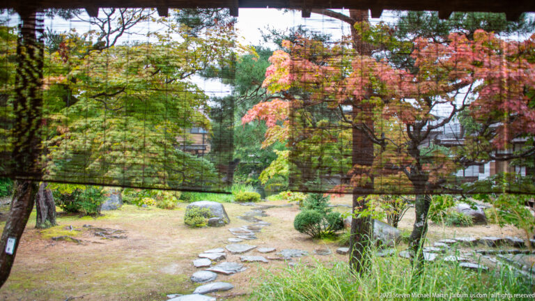 Mossy courtyard garden with stepping-stone path, maple trees, clipped shrubs, rocks, and autumn foliage.