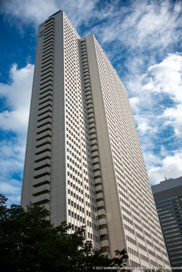 Low-angle view of a pale rectangular high-rise with repetitive windows and vertical balcony bands.