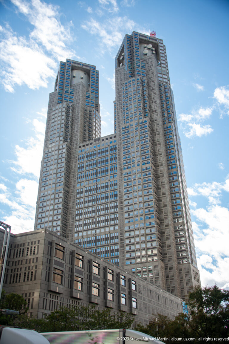 Wide street view of the Tokyo Metropolitan Government Building’s twin towers and large civic base.