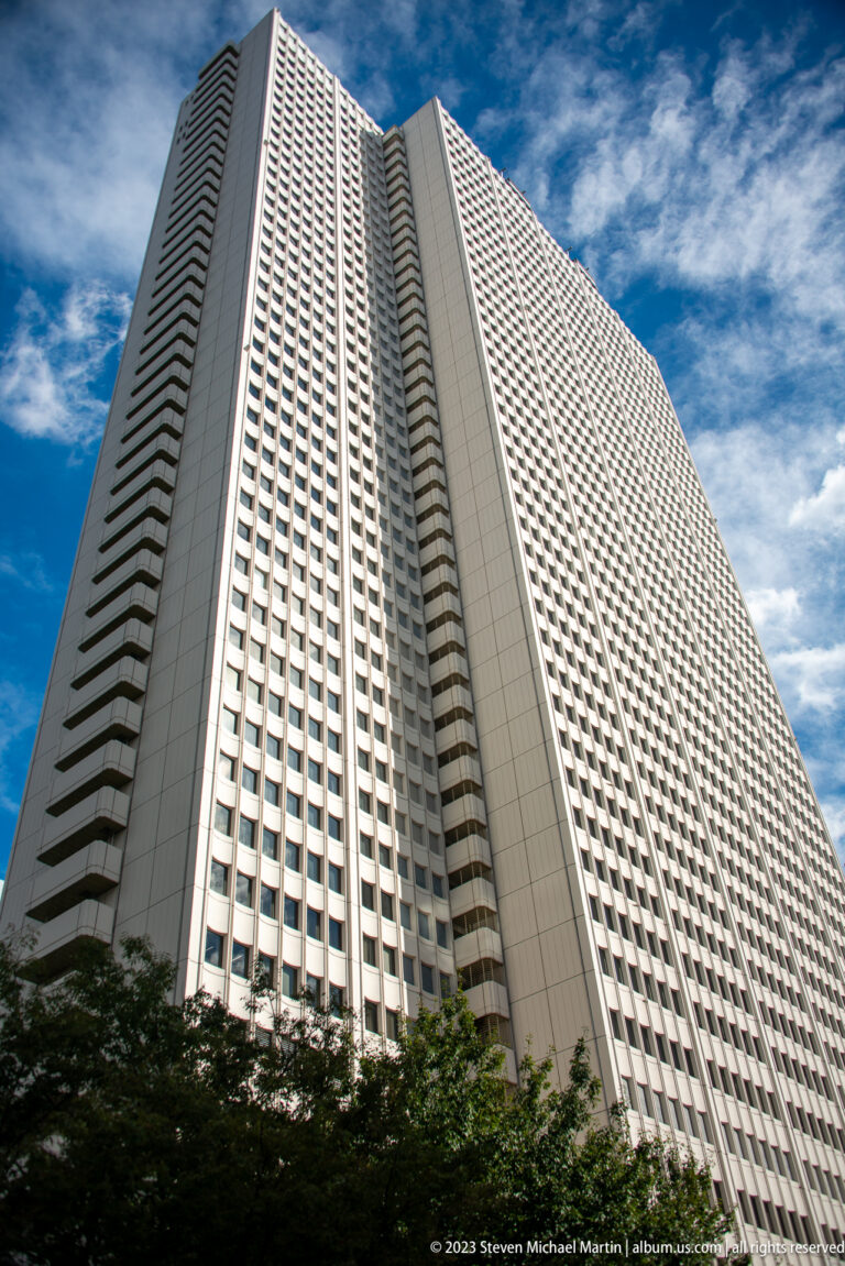 Steep low-angle view of a broad pale high-rise with a dense square-window grid and darker side bands.