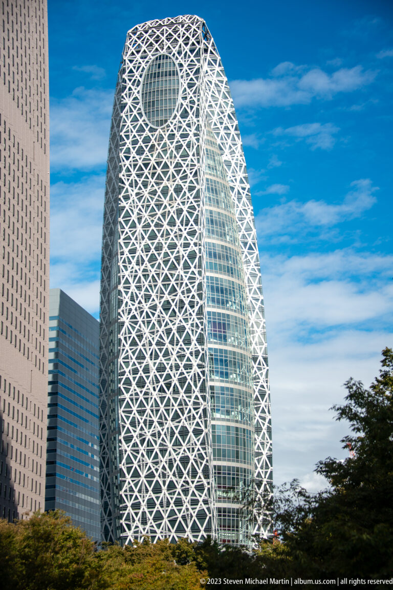 Full street-level view of the Mode Gakuen Cocoon Tower with its white diagrid and oval crown opening.