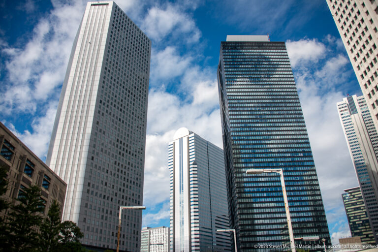 Upward view of a dark glass office tower framed by pale high-rises in Shinjuku.