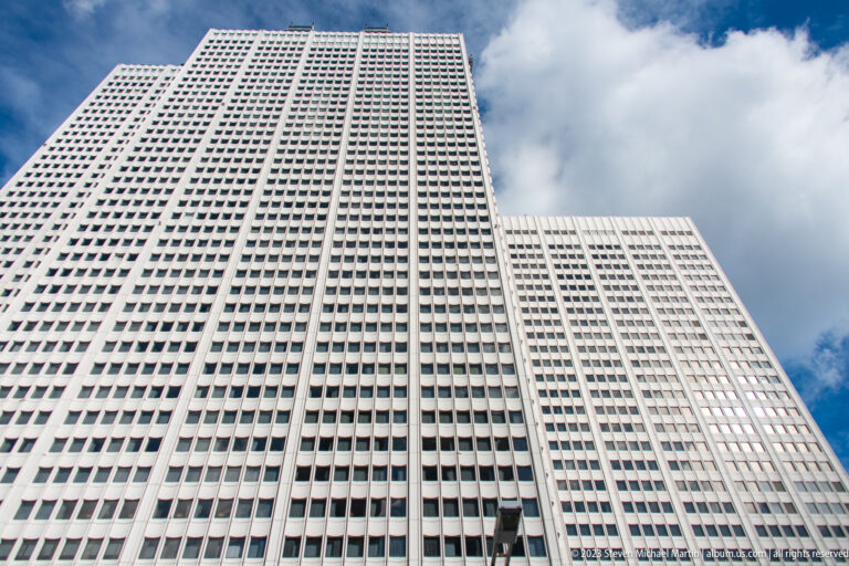 Steep upward view of a pale high-rise with a dense square-window grid and stepped wings.