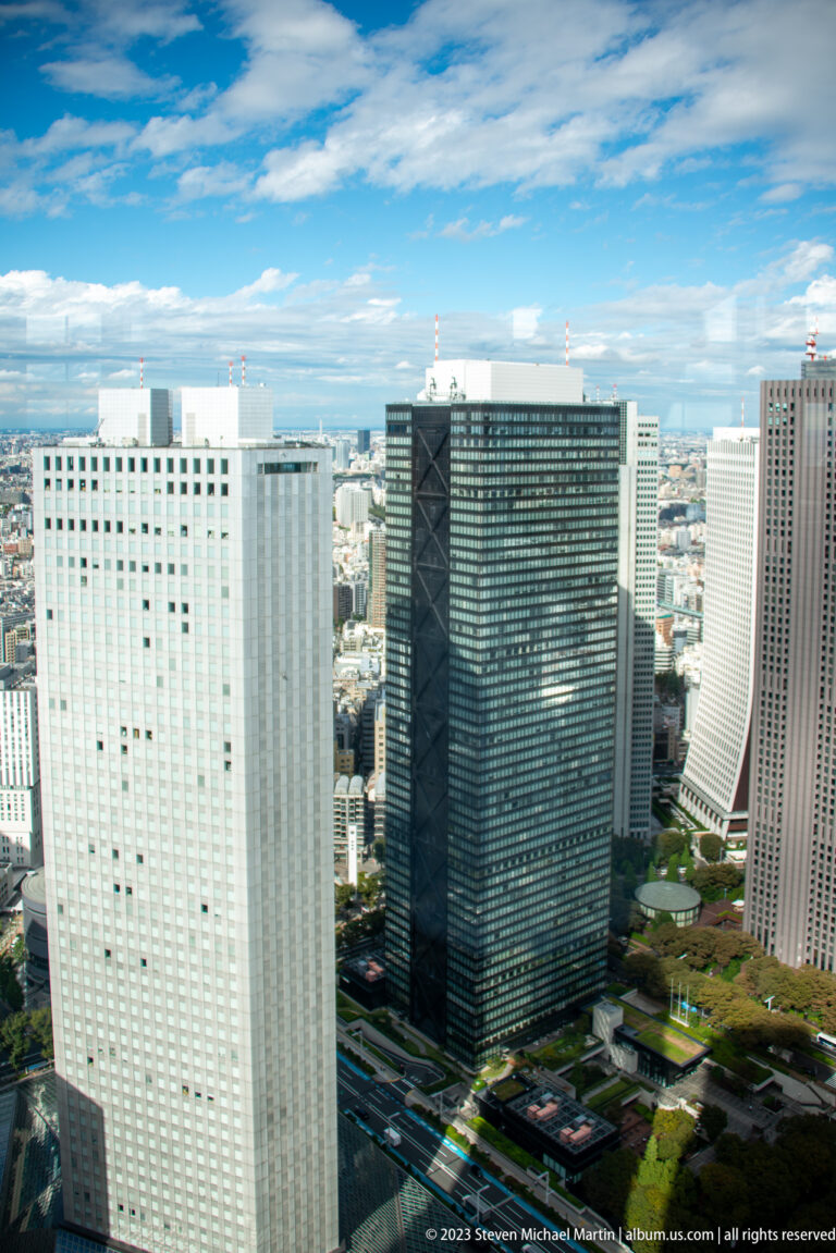 Elevated view of three Shinjuku office towers with dense Tokyo development extending behind them.