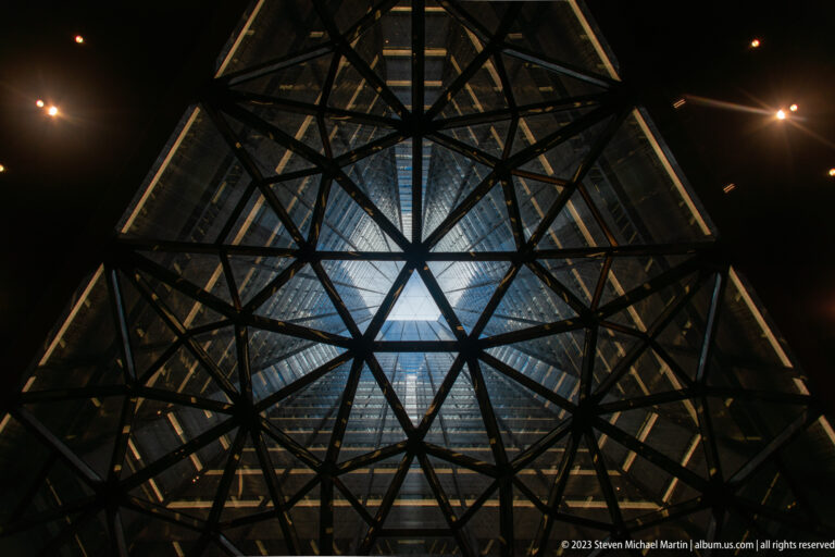 Vertical interior view of converging steel trusses and illuminated glazing beneath the observation-deck roof.